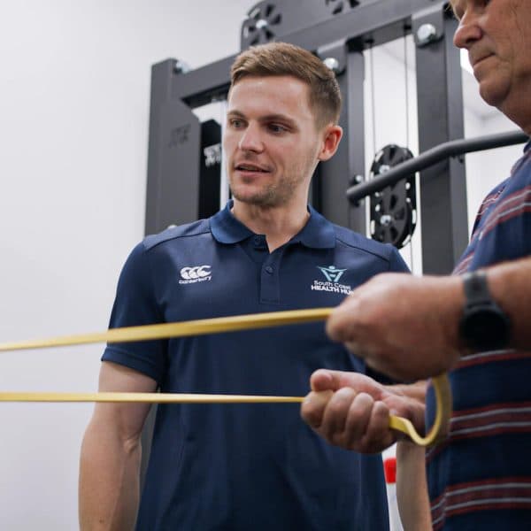 Exercise physiologist coaching a client through a resistance band exercise in the gym